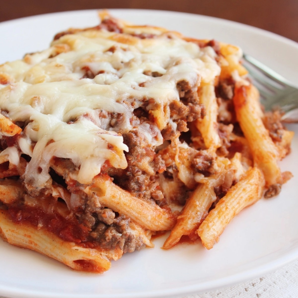 A warm, comforting slice of Cheesy Beef &amp; Penne Bake, oozing with cheese, served hot.
