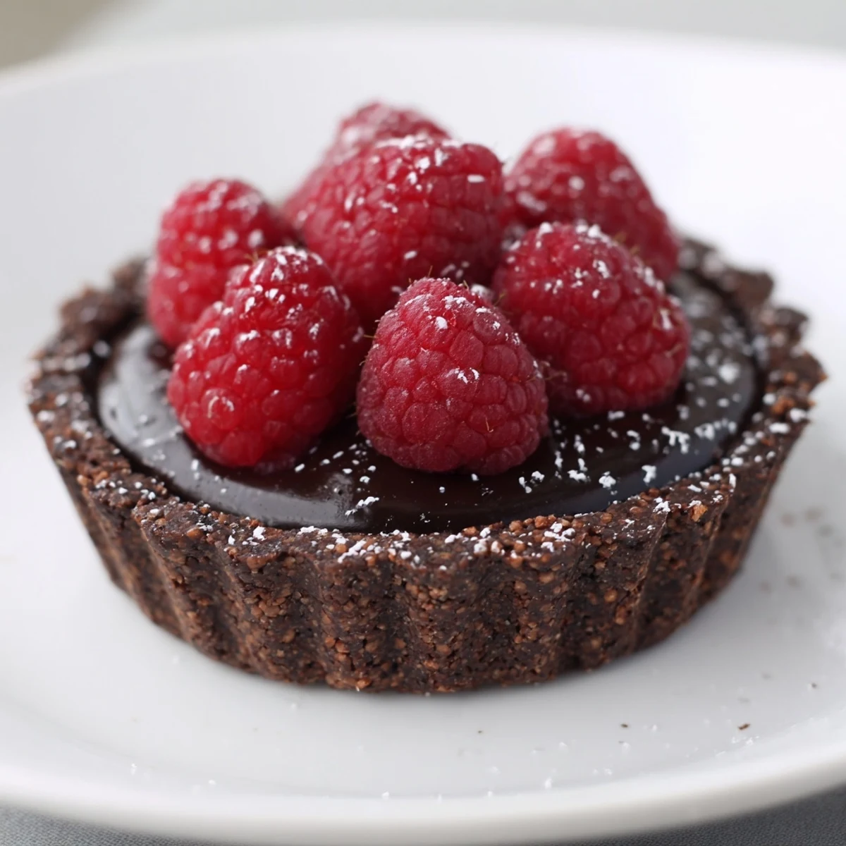 Close-up of a dark chocolate and raspberry tart; imagine creamy ganache and fresh fruit.