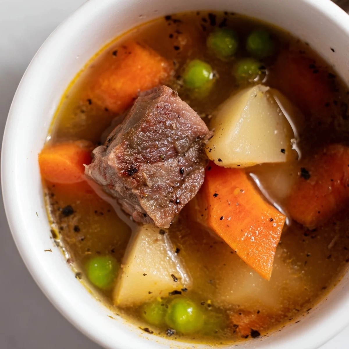 Close-up of a ladle serving Beef Vegetable Soup with Potatoes and Peas, revealing sweet green peas and diced potatoes.