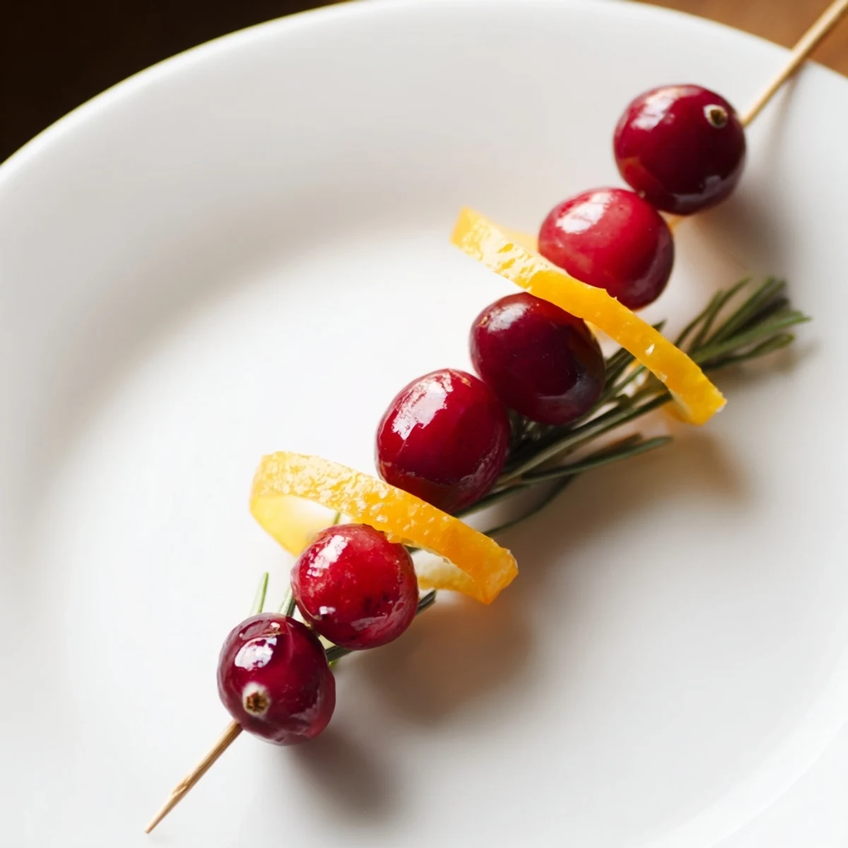 Festive cranberry garnish with orange zest and rosemary on a wooden board.