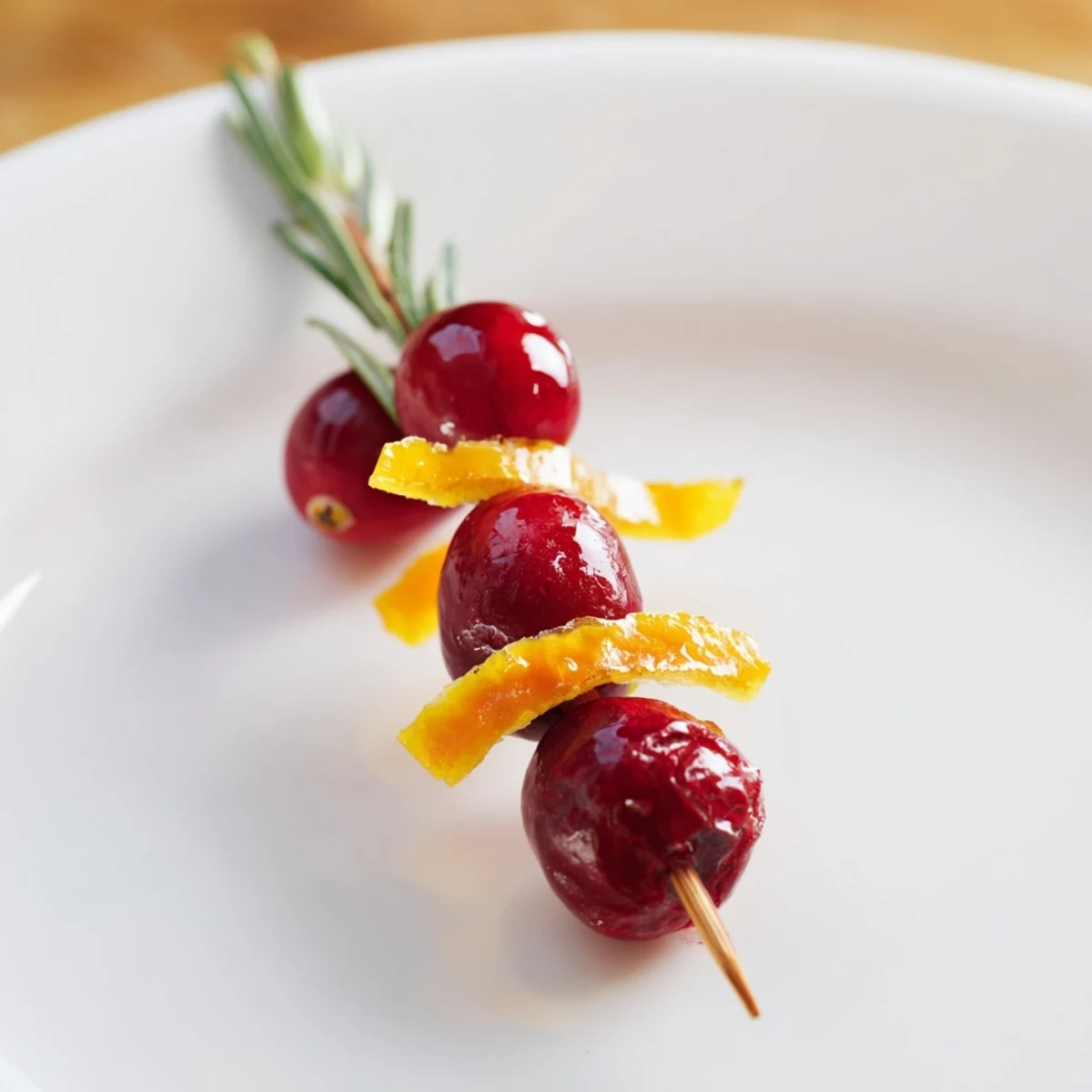 Glossy cranberry garnish recipe with orange zest and rosemary for drinks.