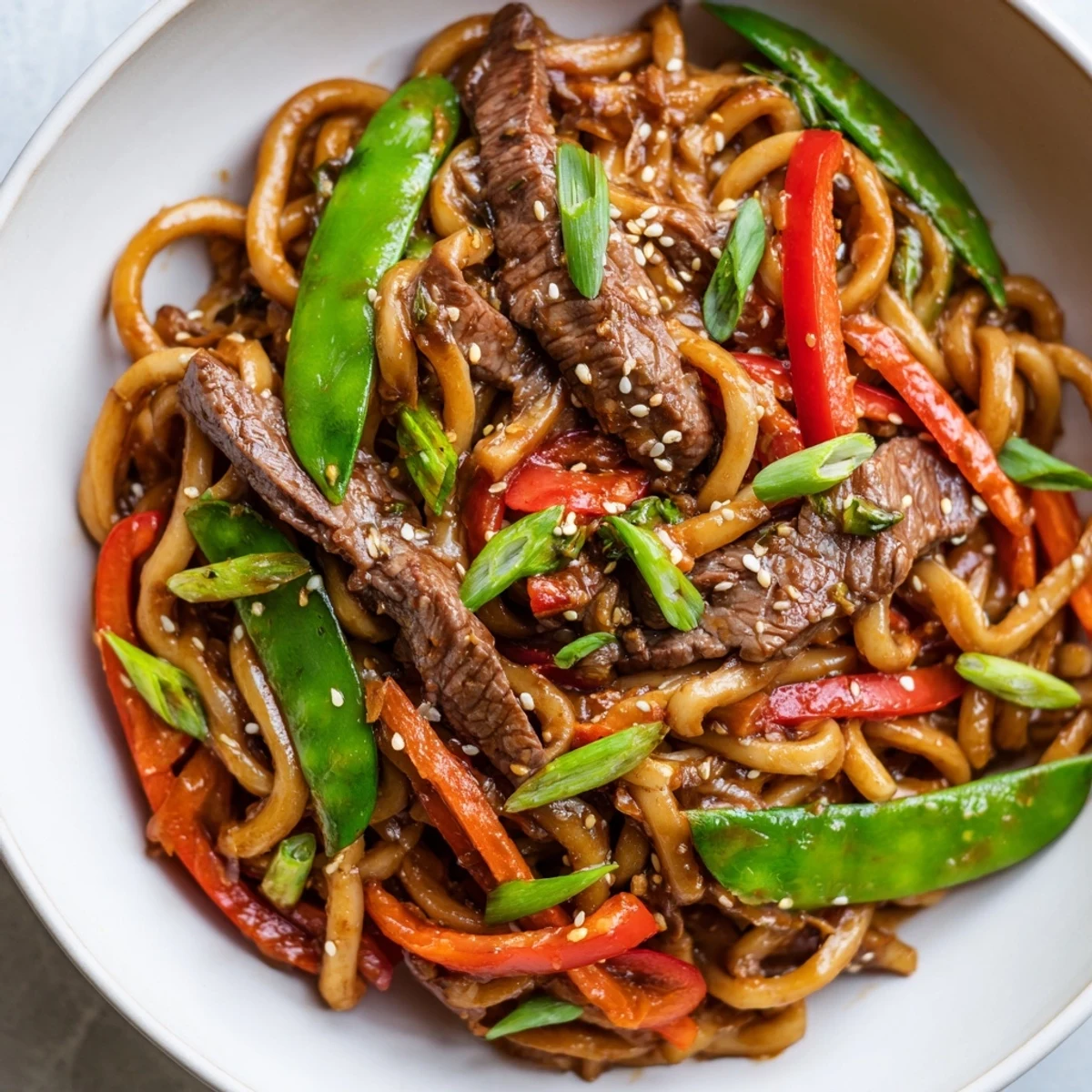 Tender beef strips and chewy udon noodles in a spicy sauce, garnished with sesame seeds and fresh scallions.