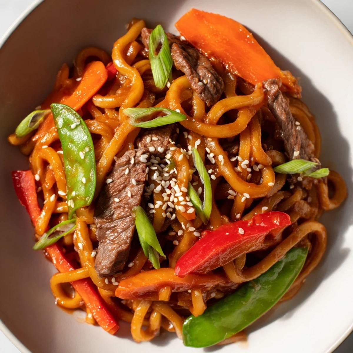 Steam rises from a serving of Spicy Beef Stir Fry with Udon Noodles, paired with chopsticks and a small bowl of soy sauce.