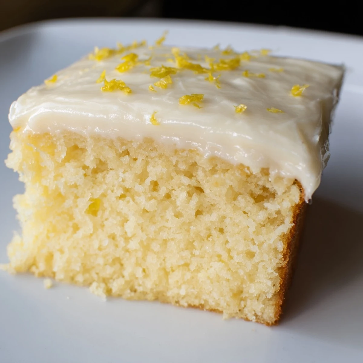 A single slice of moist lemon cake drizzled with tangy cream cheese frosting, ideal for an afternoon dessert or teatime.