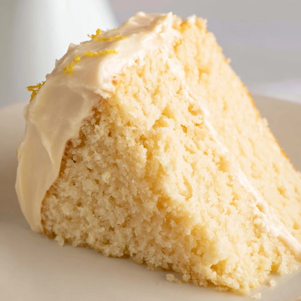 Golden lemon cake slice topped with fluffy cream cheese frosting and fresh lemon zest, ready to serve with tea or coffee.