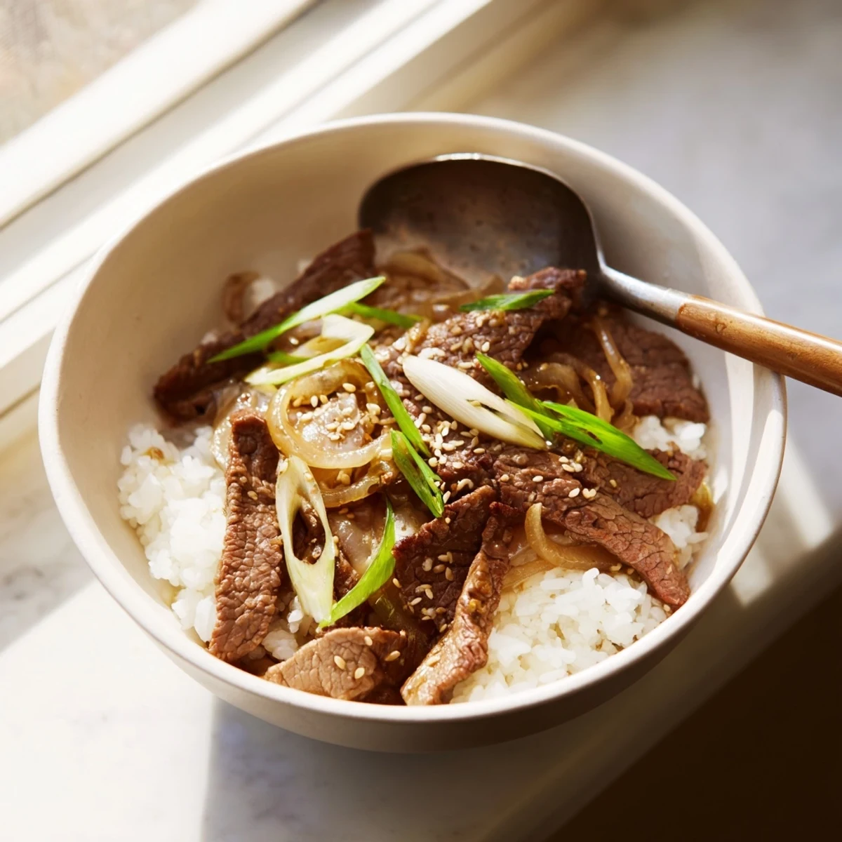 Tender beef slices with caramelized onions simmer in a rich, umami-packed sauce over a mound of perfectly cooked steamed rice.  