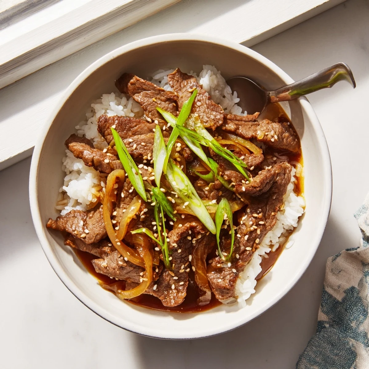 A cozy bowl of juicy beef and onions in a glossy sauce, served over fluffy rice and garnished with fresh green onions.
