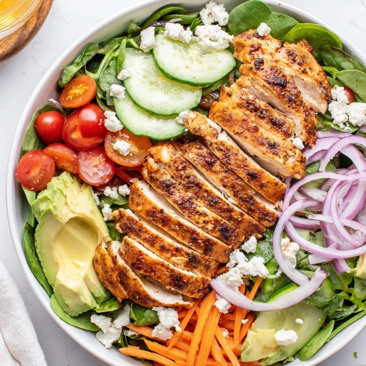 Sliced cucumbers, shredded carrots, and creamy avocado are artfully arranged in a glass meal prep container for this Chicken Meal Prep Salad.