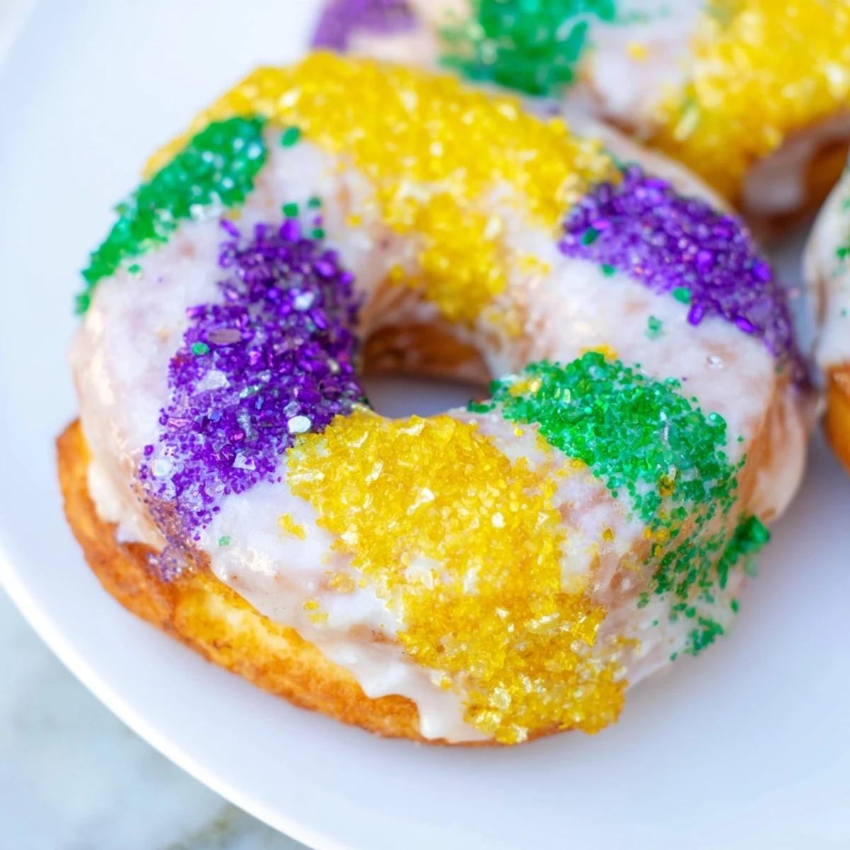 Freshly fried Mardi Gras Donuts with a glossy vanilla glaze, dusted with purple, green, and yellow sparkling sugars.
