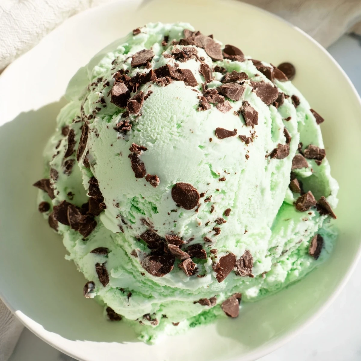 Homemade St. Patricks Day Mint Chocolate Chip Ice Cream scoops into a bowl, showcasing creamy green texture with plenty of chocolate chips. 