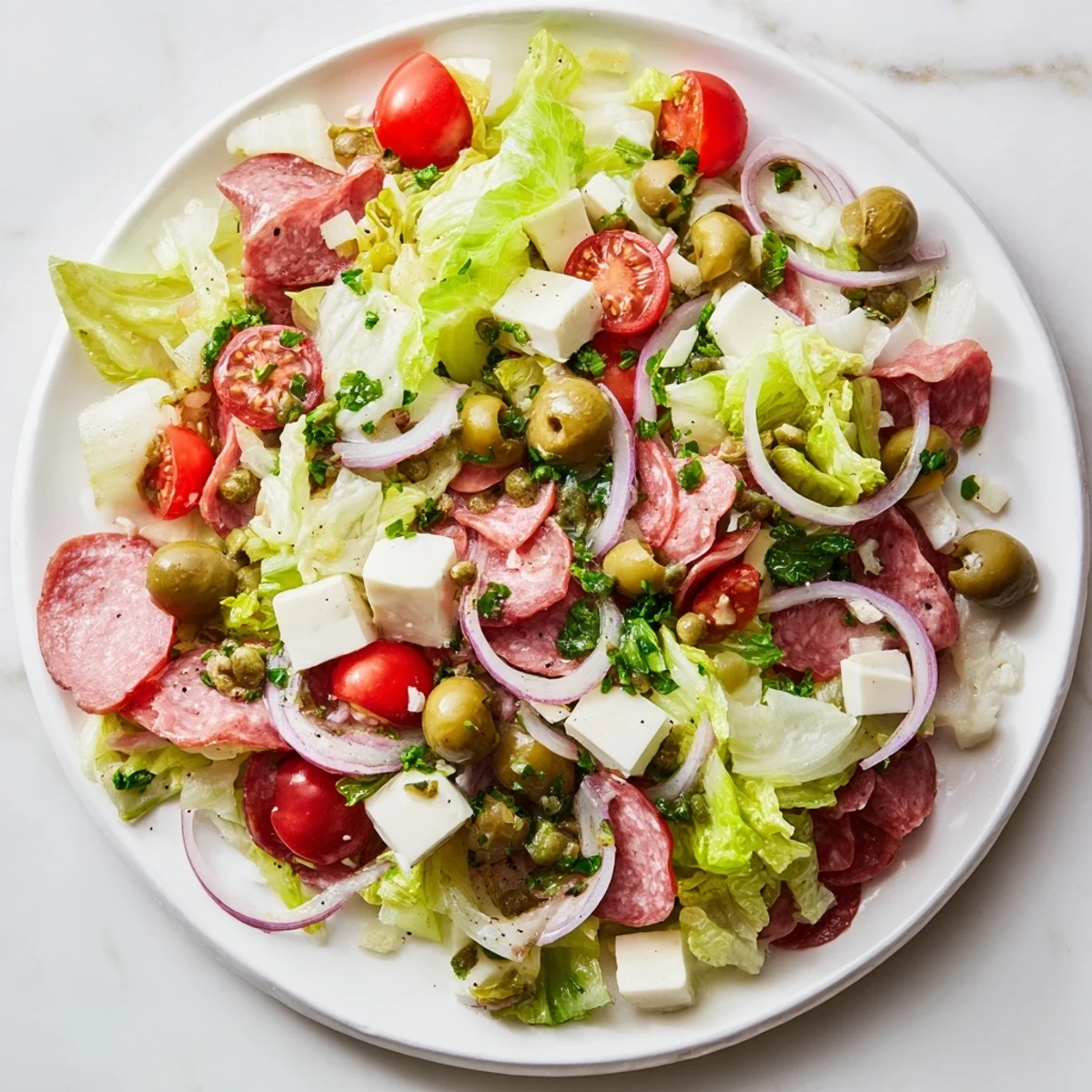 Savory New Orleans Muffuletta Salad served in a white bowl, showcasing tangy giardiniera, mozzarella cubes, and a zesty Italian dressing drizzle.  