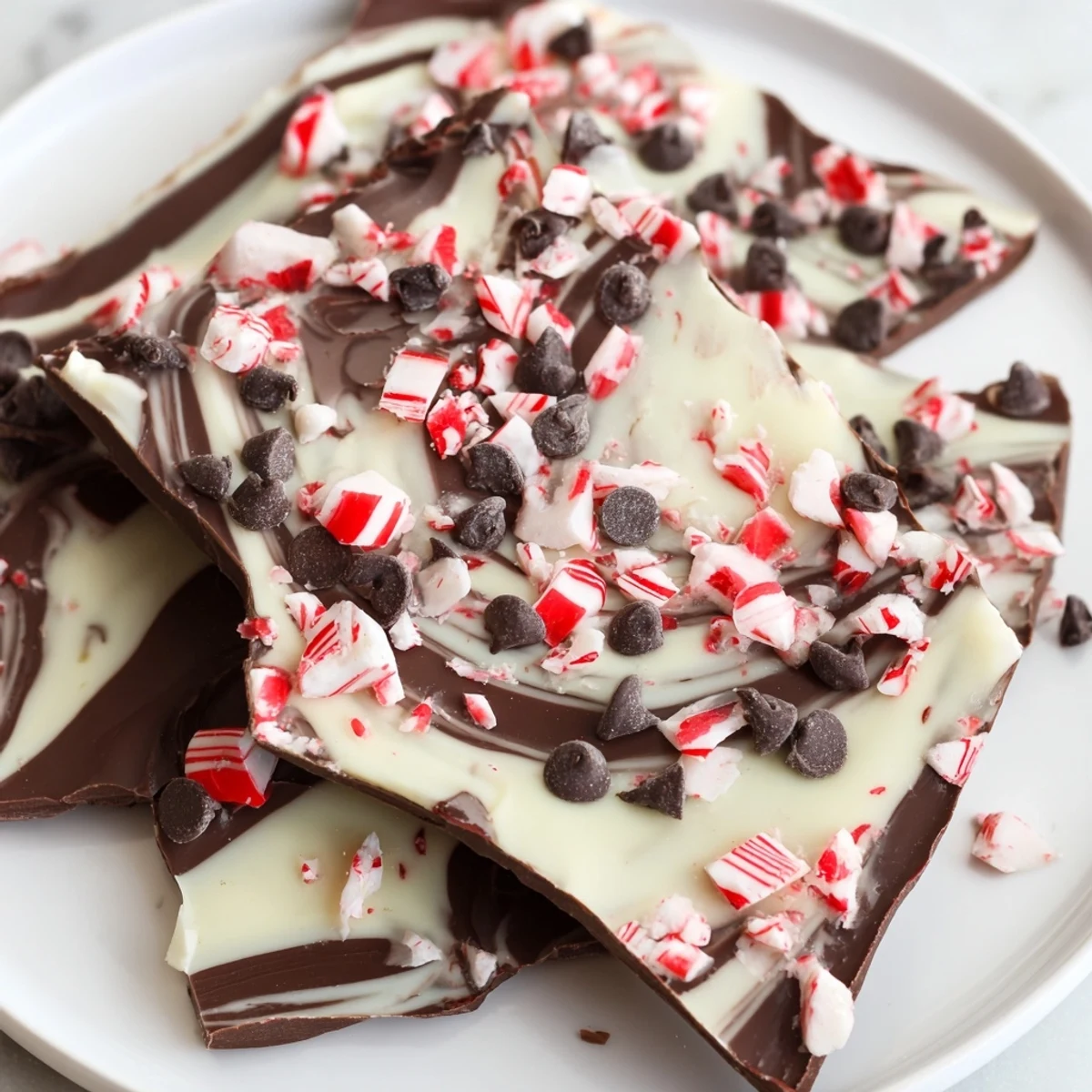 Shards of glossy dark chocolate with creamy white swirls and crushed candy cane pieces, ideal for holiday snacking.