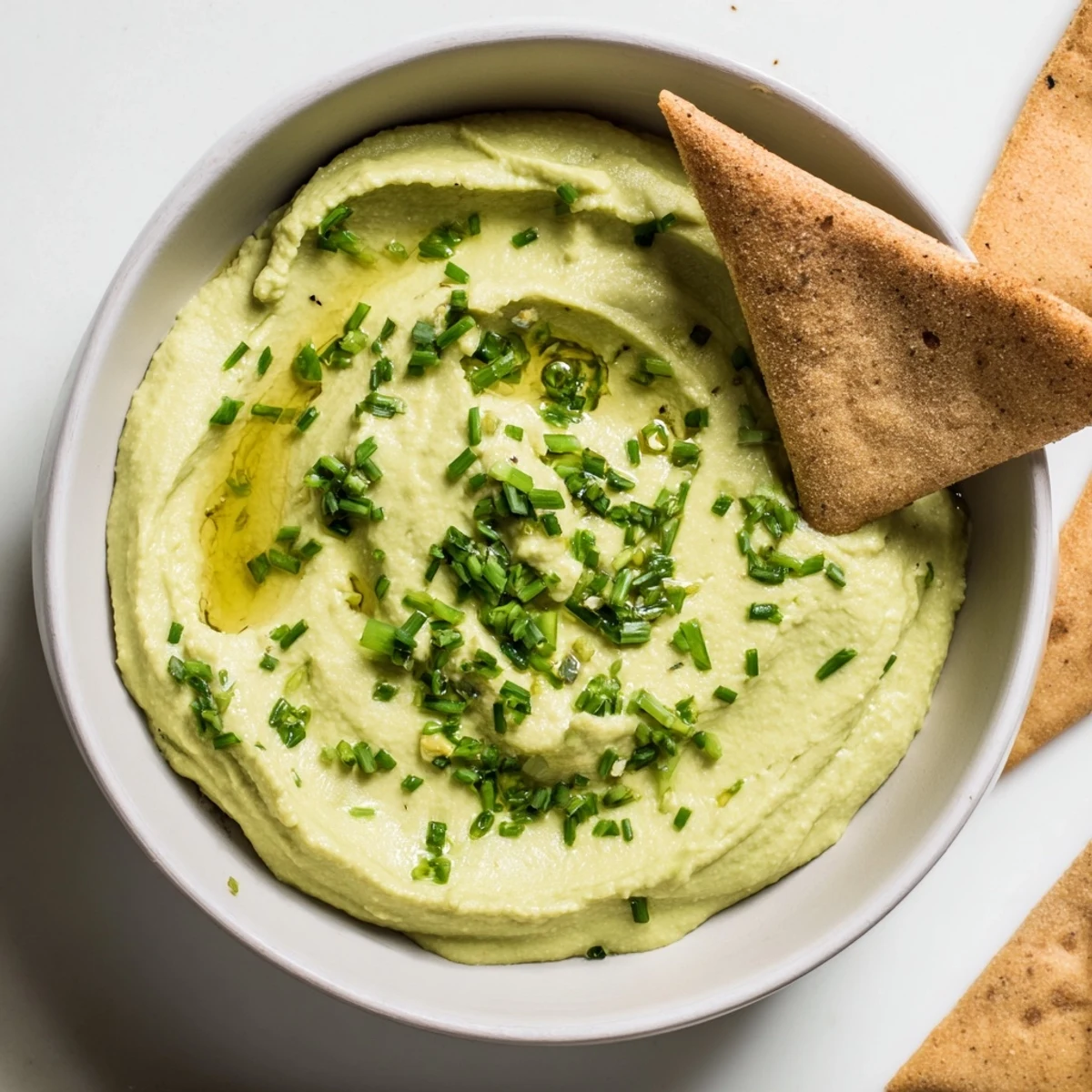 Fresh avocado hummus dip with cilantro and lime, served alongside warm pita chips for dipping.  