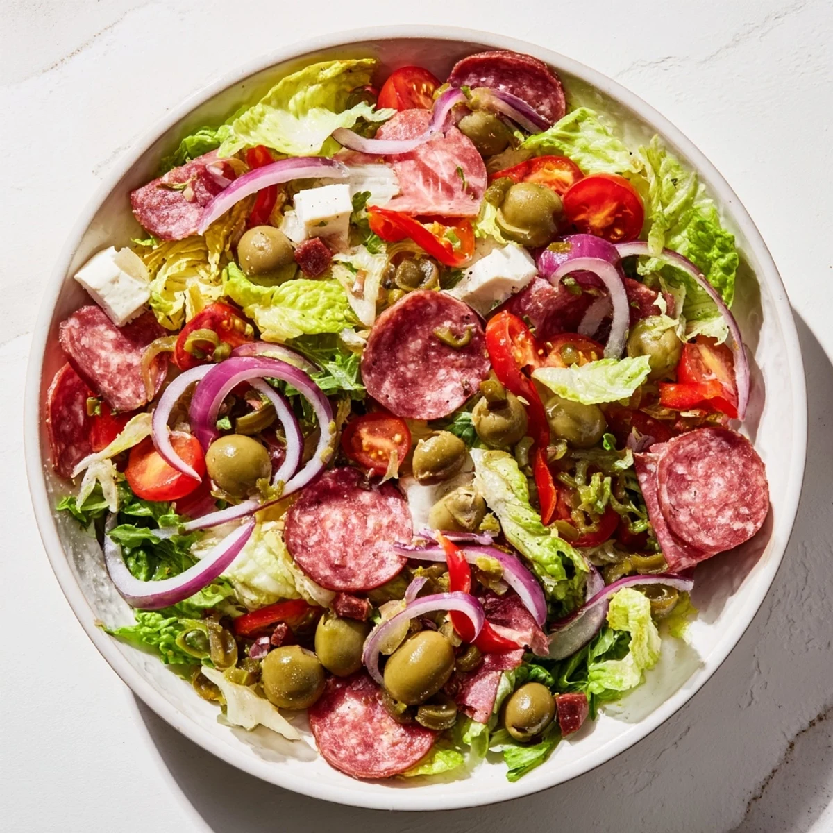 Vibrant bowl of New Orleans Muffuletta Salad featuring marinated olives, cured meats, and provolone with tangy dressing.