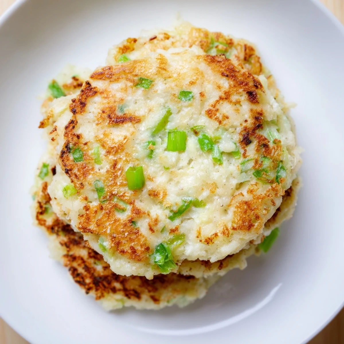 Freshly fried Irish Boxty Potato Pancakes with visible scallion pieces, resting on a plate with a dollop of sour cream.