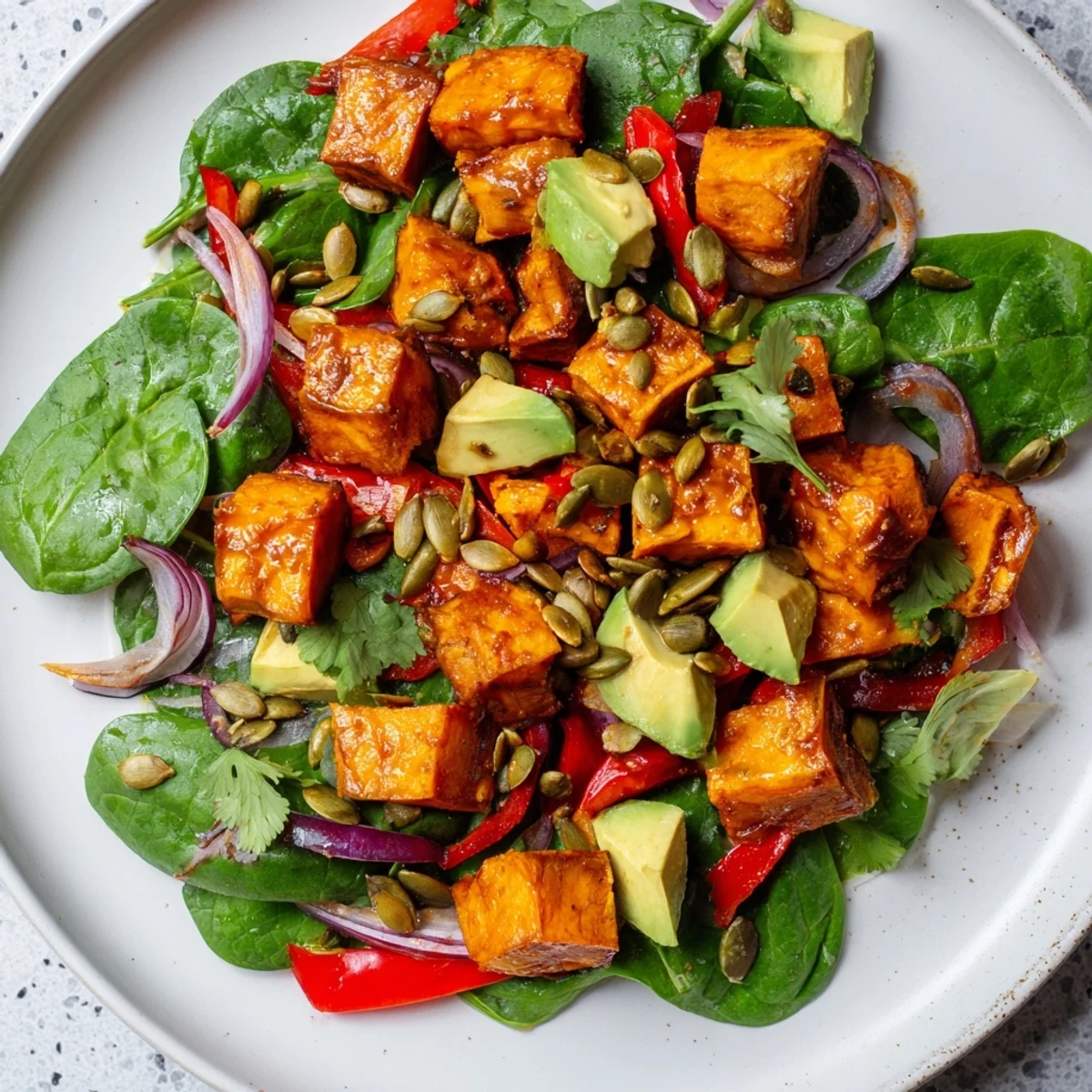 Golden roasted sweet potato salad with lime dressing on a white plate, topped with pumpkin seeds and fresh cilantro.