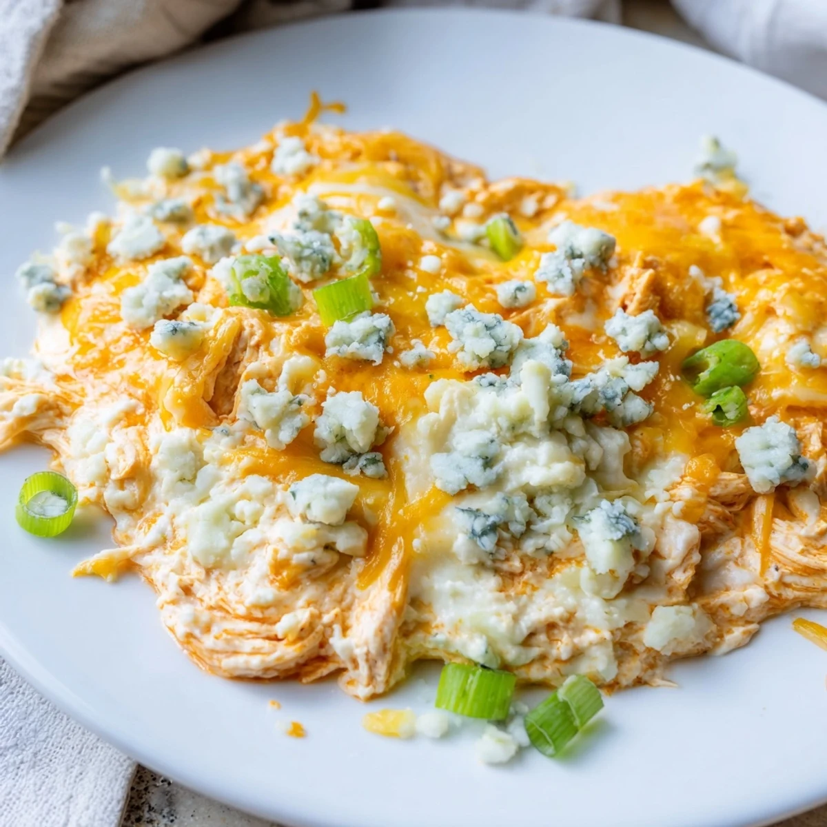 Close-up of Keto Buffalo Chicken Dip in a baking dish, melted mozzarella and cheddar bubbling over a creamy, spicy chicken mixture.