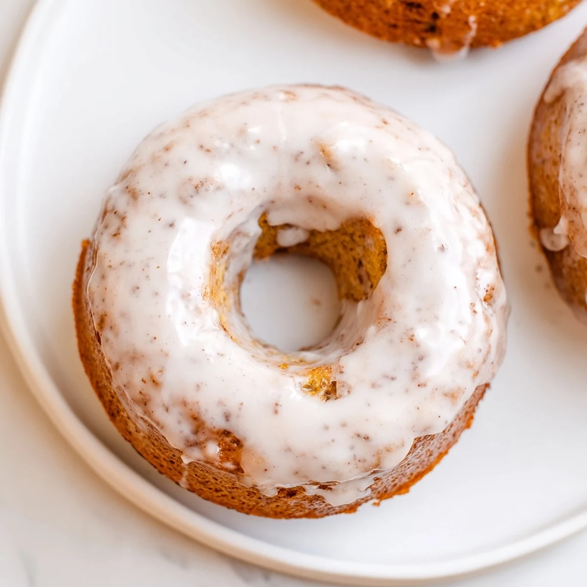 Twelve freshly baked banana bread donuts arranged on a wire cooling rack with ripe bananas nearby.