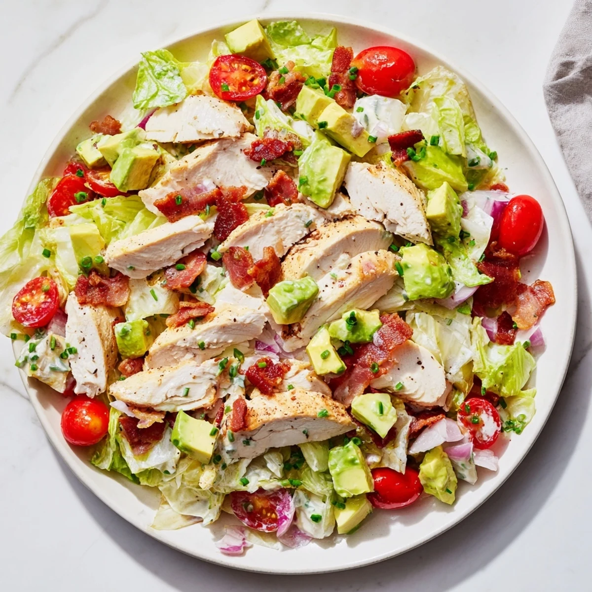 Close-up of BLT Chicken Salad featuring sliced chicken, crispy bacon crumbles, halved cherry tomatoes, avocado, and chopped romaine with creamy dressing.