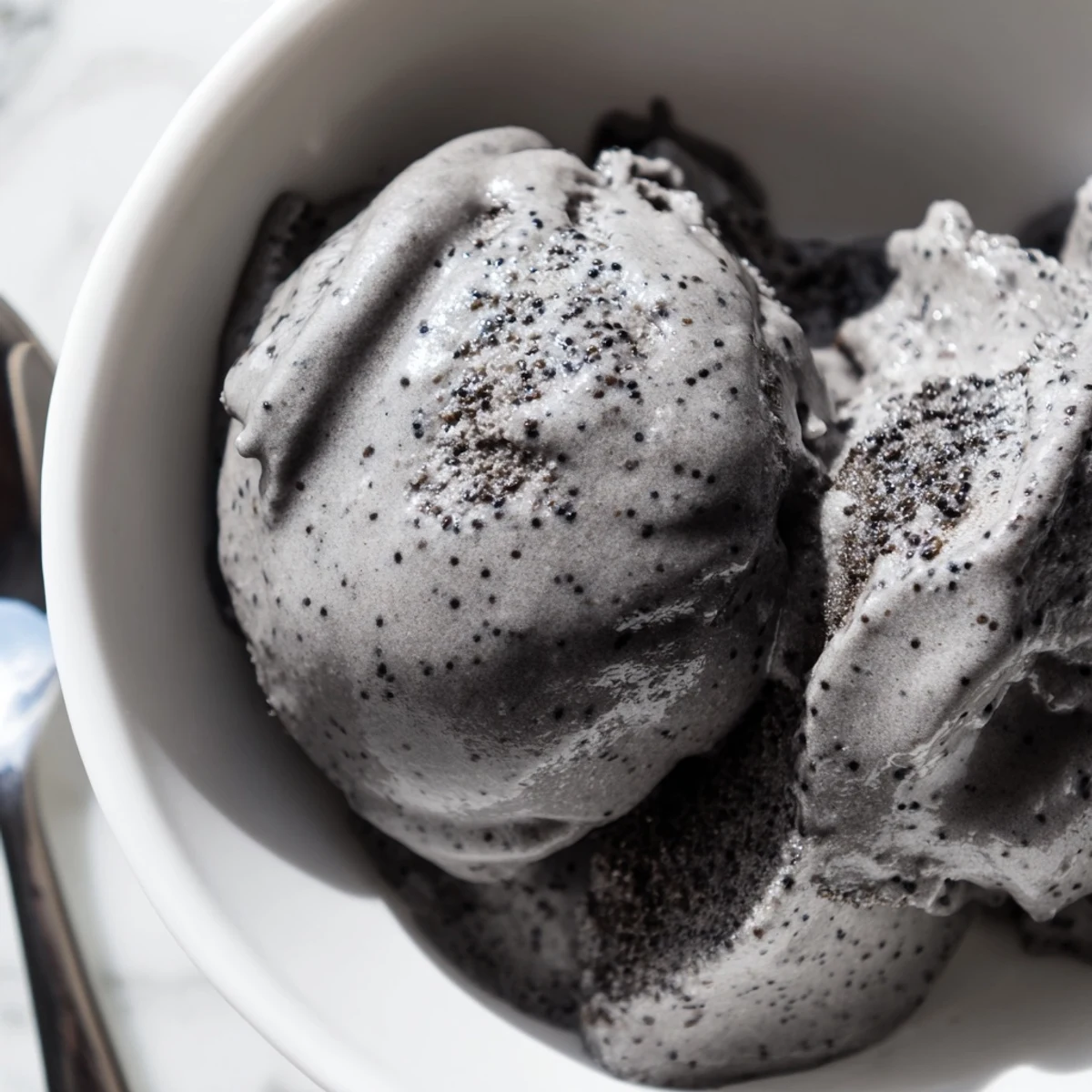 Creamy Toasted Black Sesame Ice Cream scooped into a chilled bowl with toasted sesame seeds sprinkled on top.