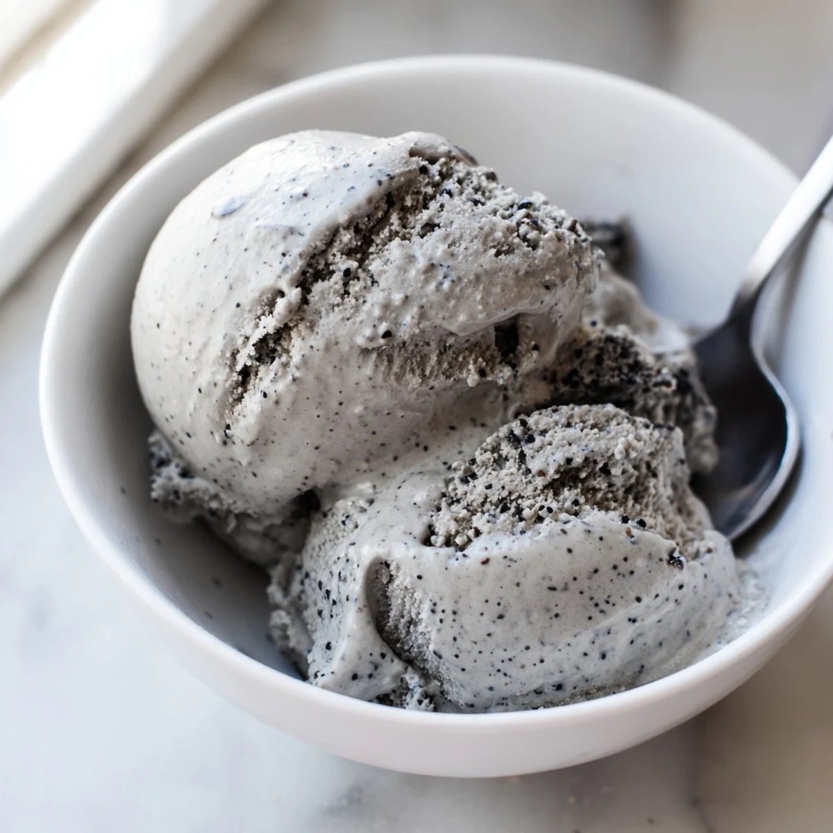 Close-up of Toasted Black Sesame Ice Cream with a smooth texture and dark speckles, served on a waffle cone.