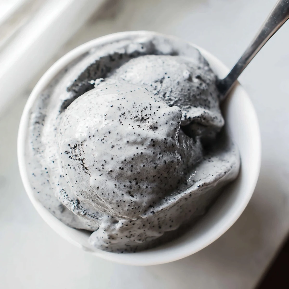 Scoop of rich Toasted Black Sesame Ice Cream melting slightly on a dessert plate with a honey drizzle.