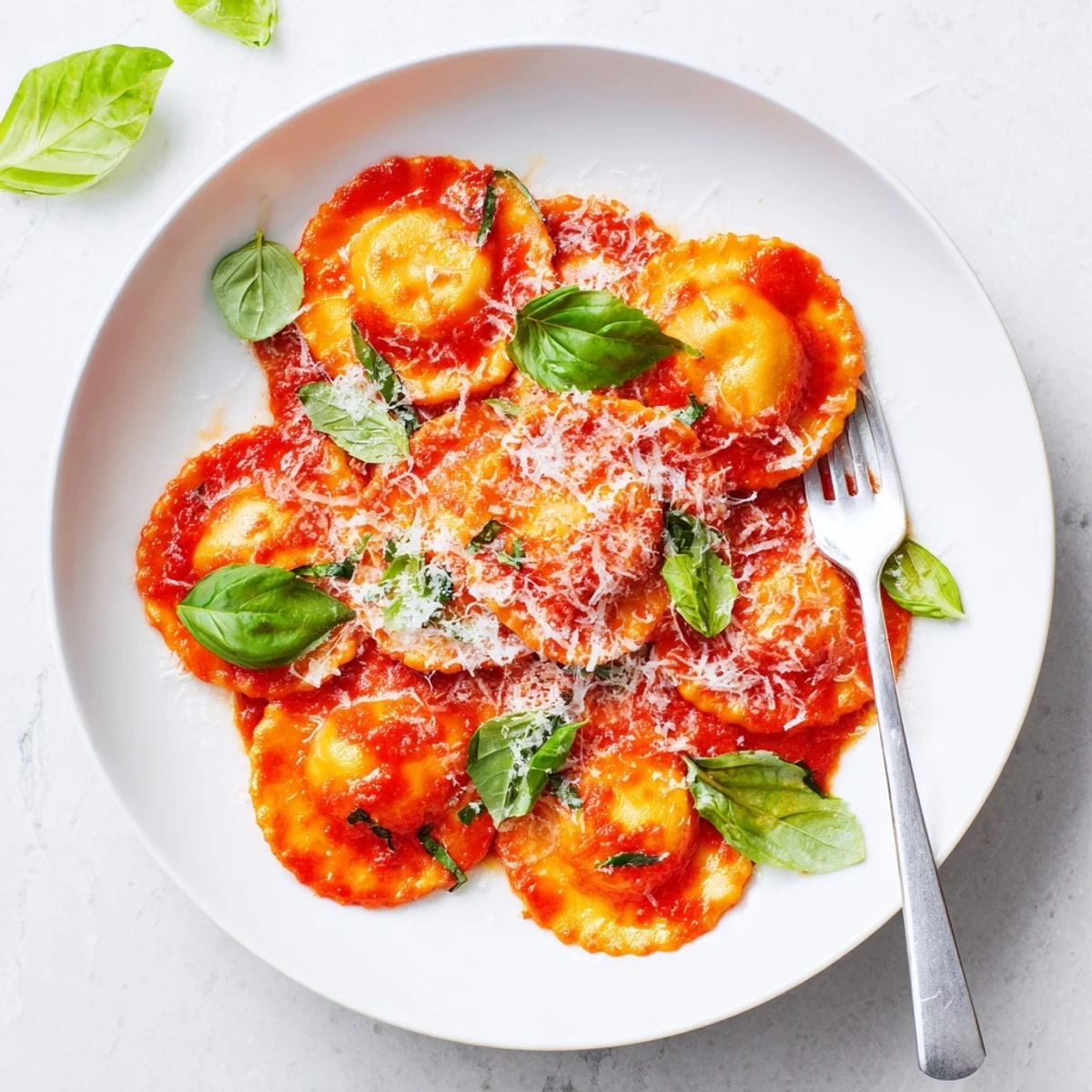 Steamed cheese ravioli tossed in a vibrant tomato-basil sauce, garnished with fresh basil and grated Parmesan cheese.