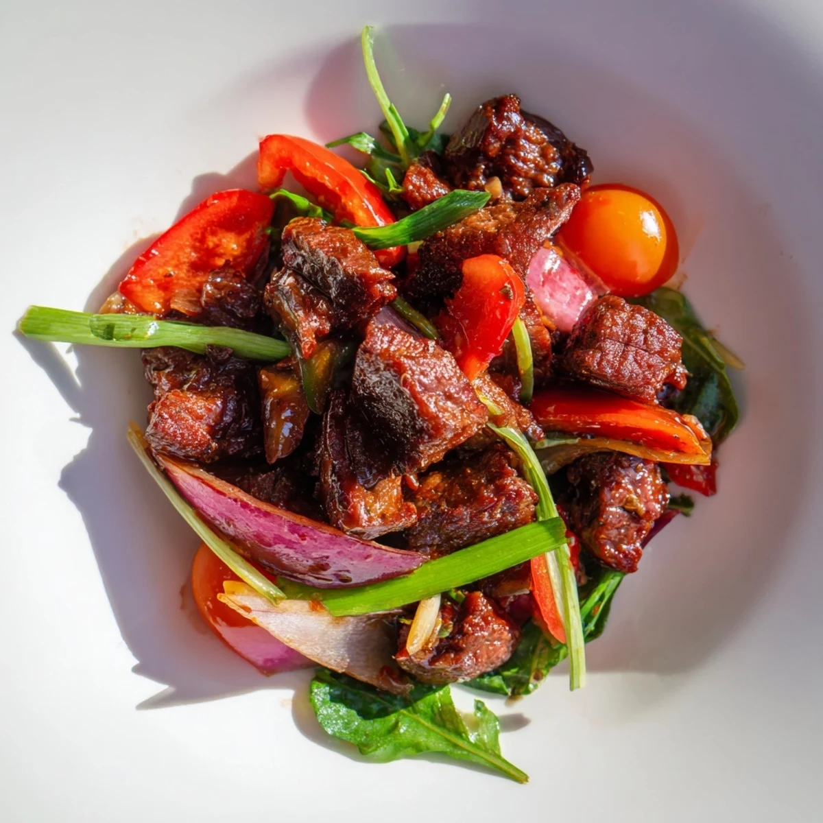 Freshly plated Vietnamese Shaking Beef over greens and tomatoes, with a tangy lime dipping sauce and warm steamed rice nearby.
