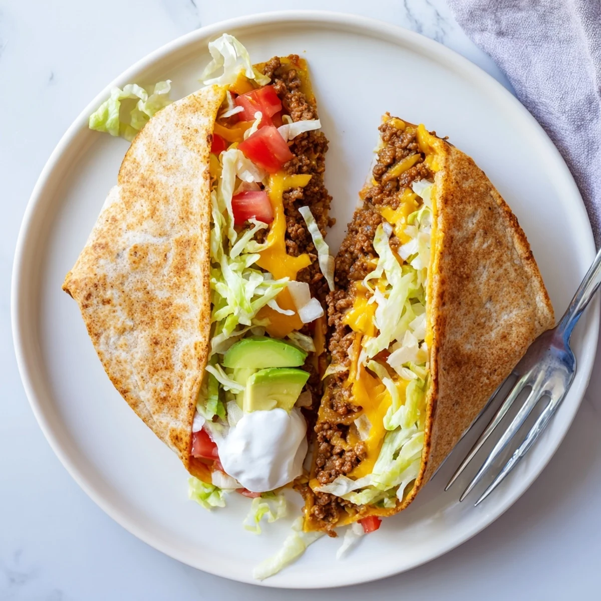 Golden keto crunchwrap featuring seasoned beef, melted cheddar, fresh lettuce, and creamy sour cream folded inside a crispy low-carb tortilla