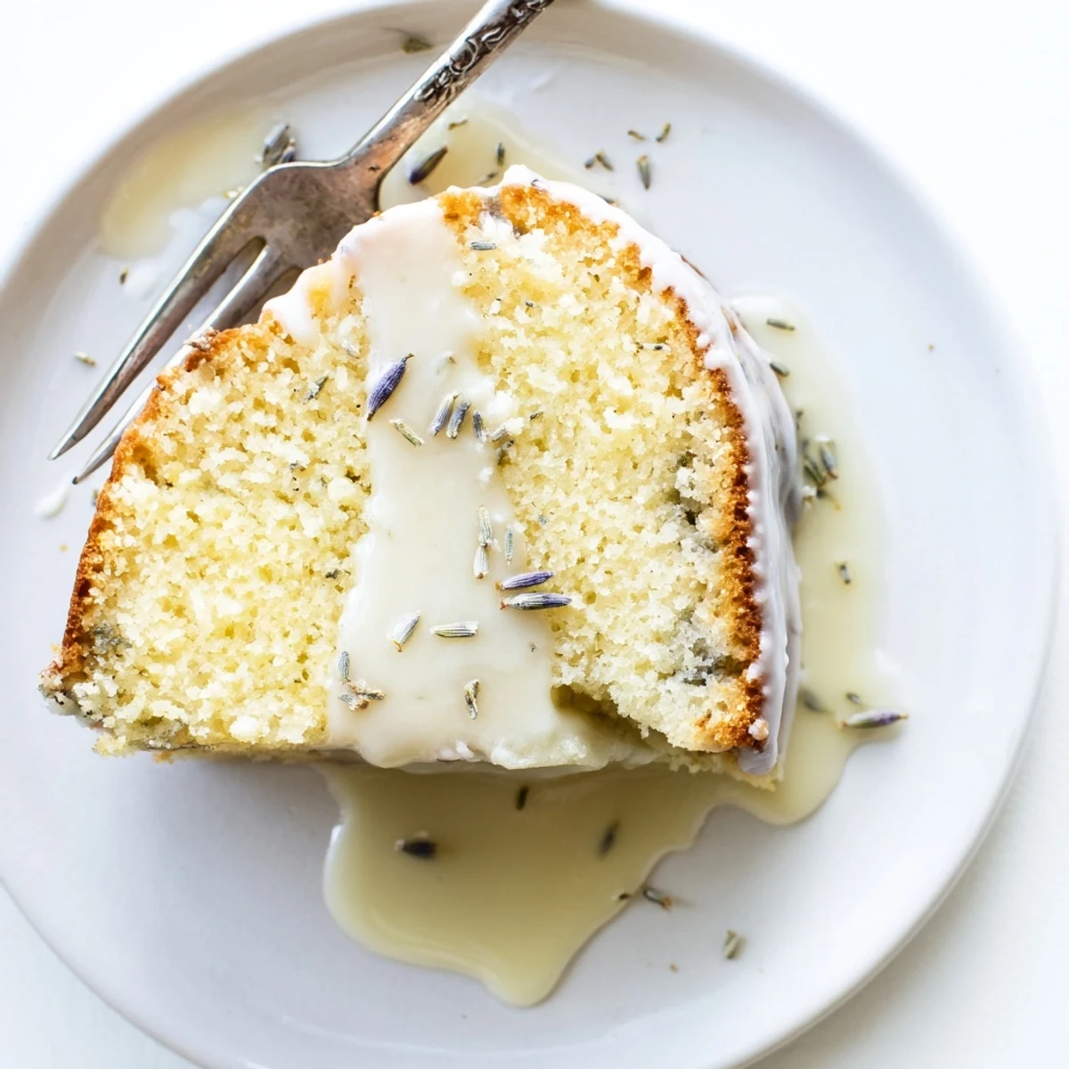 Moist lemon lavender cake slice on a white plate with fresh lavender sprigs nearby