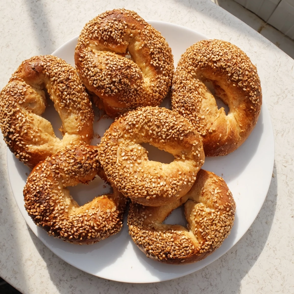 Homemade sesame bread rings coated in toasted seeds on wooden serving board with olive dip