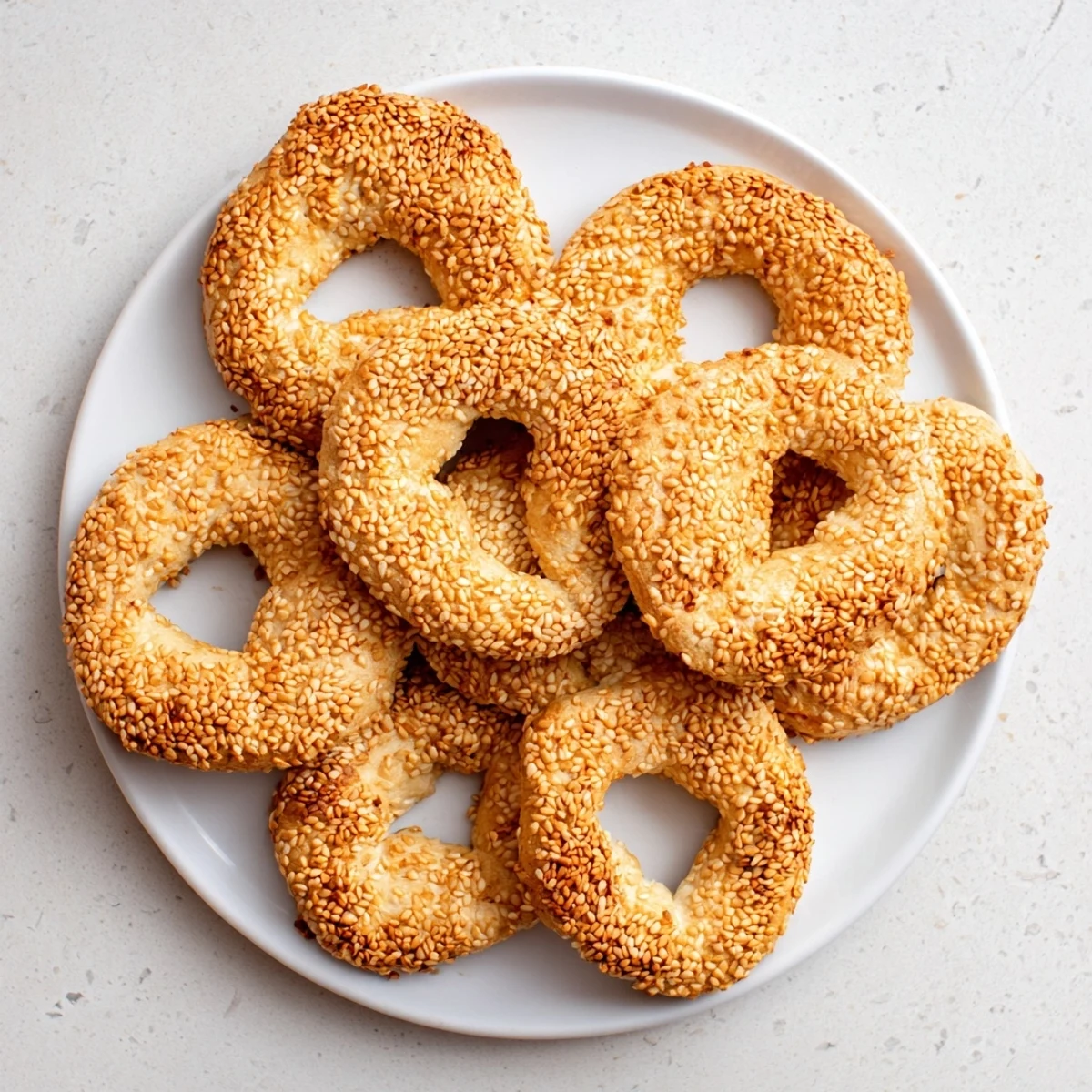 Freshly baked sesame bread rings stacked on wire rack showing golden brown crust and white interior