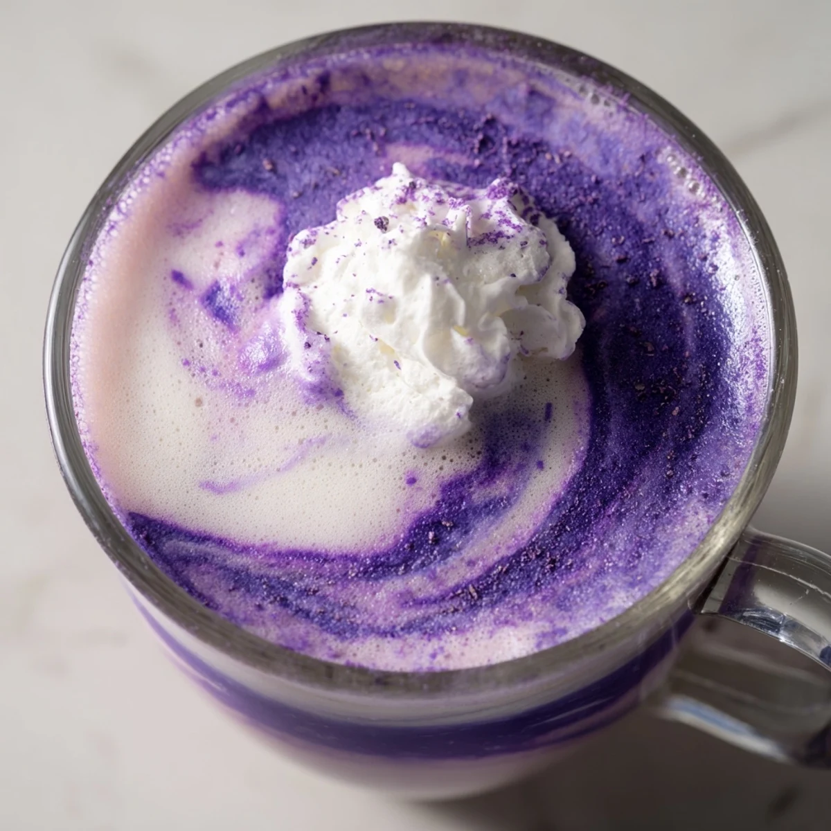 Vibrant purple ube latte with creamy foam topped with whipped cream and purple yam flakes