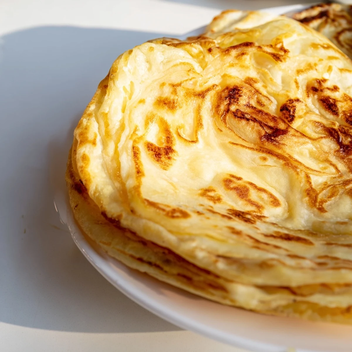 Freshly cooked Malaysian roti canai folded into triangles revealing buttery tender interior layers