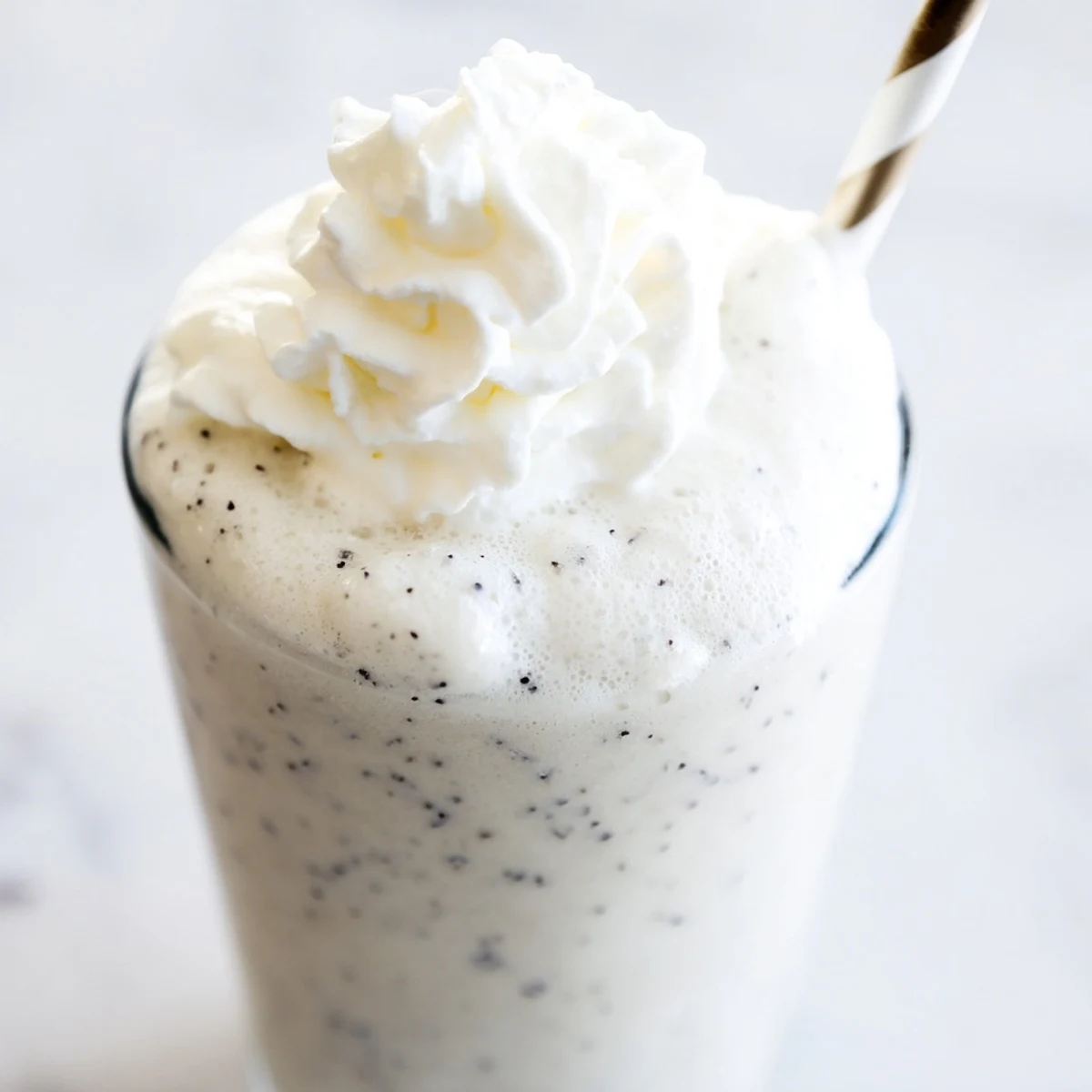 Blended vanilla bean frappuccino with visible specks and ice in a transparent glass