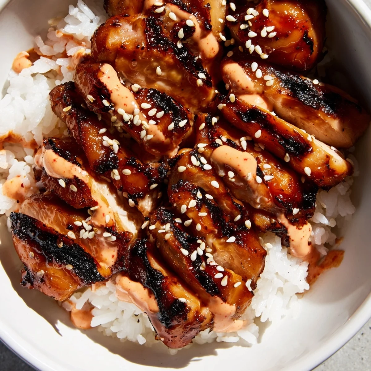 Vibrant Korean BBQ chicken bowl featuring charred glazed chicken thighs atop jasmine rice with fresh avocado, cucumbers, and purple cabbage