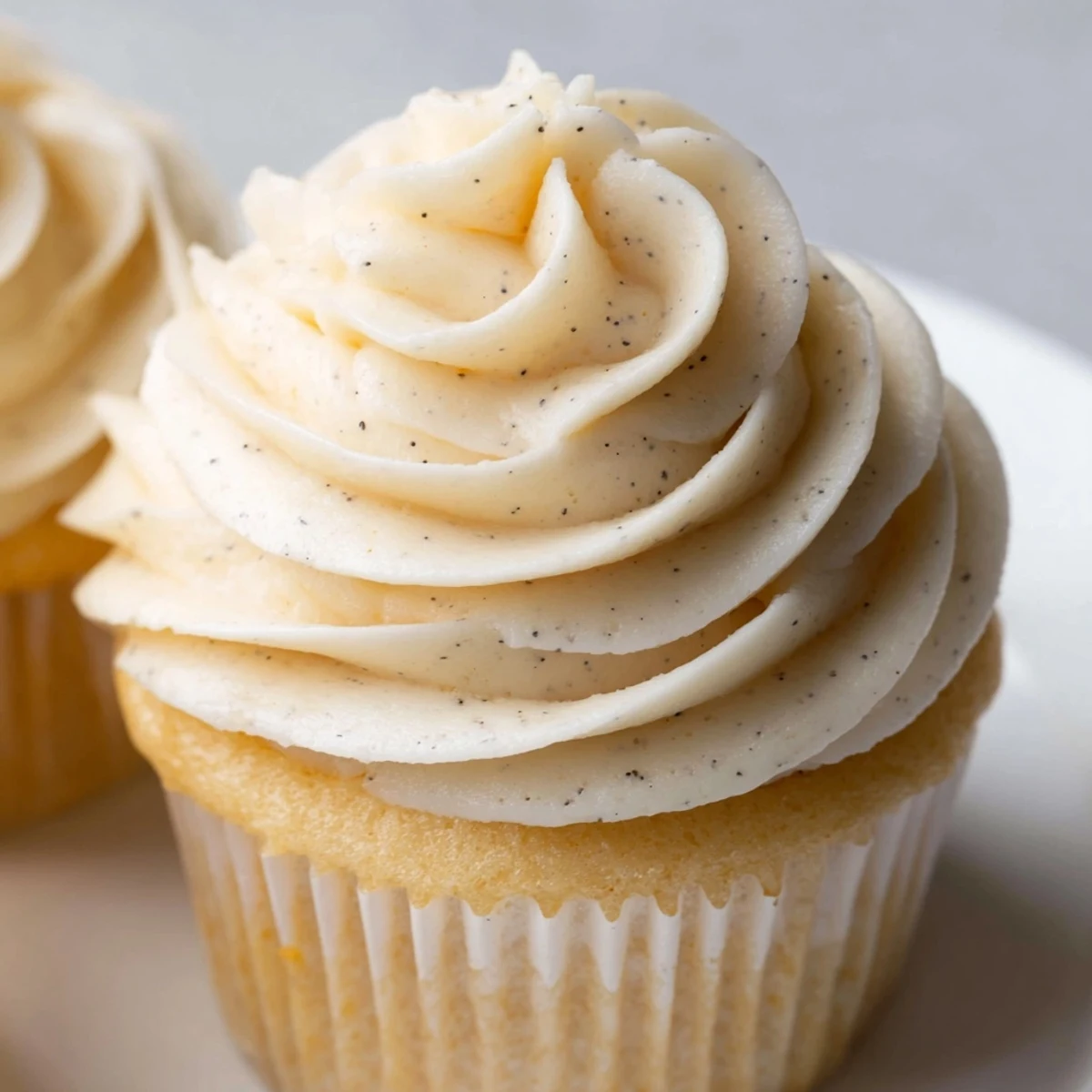 Golden vanilla cupcakes topped with creamy white buttercream frosting and colorful sprinkles on a white plate