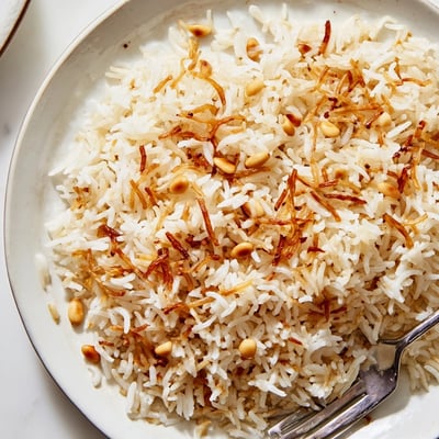 Steaming bowl of Lebanese Rice garnished with buttery pine nuts and fresh herbs